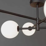Lampa sufitowa Sarius, czarna, 6-punktowa. Konstrukcja z metalowymi ramionami w kolorze czarnym, z białymi, okrągłymi kloszami. Ujęcie z bliska, ukazujące detale mocowania i kształt kloszy. Tło szare, proste.