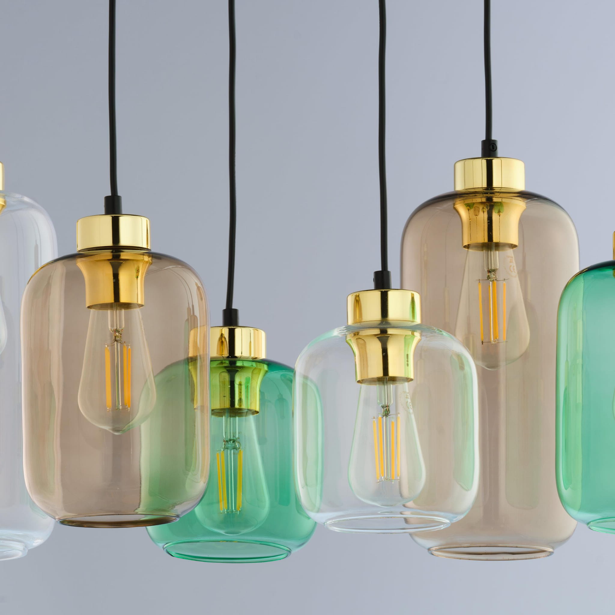 Lampa wisząca Marco Green 6-punktowa 3328 z sześcioma szklanymi kloszami w odcieniach zieleni i brązu, z metalowymi złotymi detalami. Klosze mają różne kształty i są zawieszone na czarnych przewodach, tworząc nowoczesną aranżację.