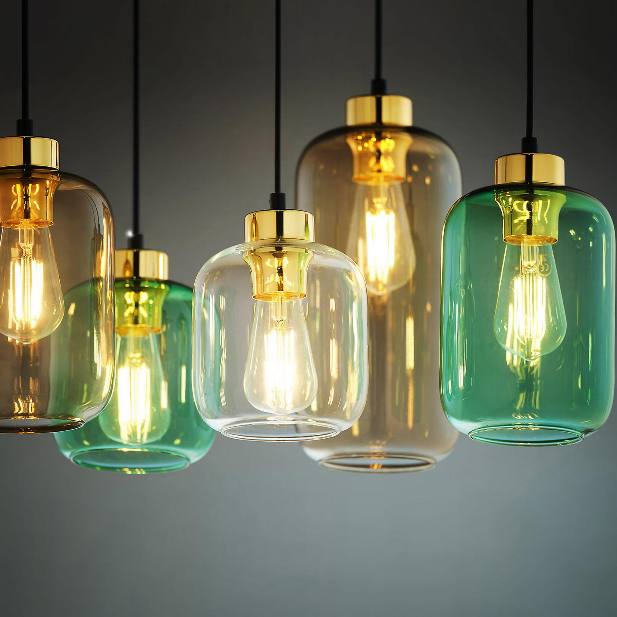 Lampa wisząca Marco Green 6-punktowa z różnokolorowymi kloszami: zielonym, przezroczystym i brązowym, z metalowymi złotymi elementami. Klosze mają różne kształty, a w środku znajdują się żarówki, emitujące ciepłe światło.