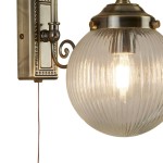 Kinkiet Belvue IP44 w antycznym mosiądzu z przezroczystą, żłobkowaną kulą. Montowany na ścianie, z widocznym przewodem. Okrągła forma lampy, elegancka konstrukcja z dekoracyjnymi detalami.