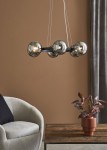Lampa wisząca Circle 6-punktowa, czarna z dymionymi kloszami, zawieszona na cienkich linkach w minimalistycznym stylu. Widoczna w aranżacji z szarym fotelem i drewnianym stolikiem, w tle ściana w odcieniu brązu.