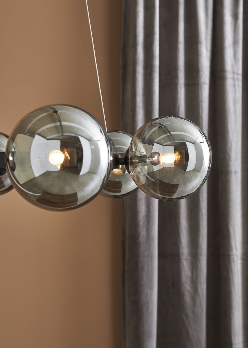 Lampa wisząca Circle 6-punktowa w kolorze czarnym z dymionymi kloszami. Produkt zawiera sześć szklanych kul, z których każda mieści żarówkę, zawieszonych na cienkim przewodzie. Ujęcie z góry, w tle zasłona w odcieniu szarości.
