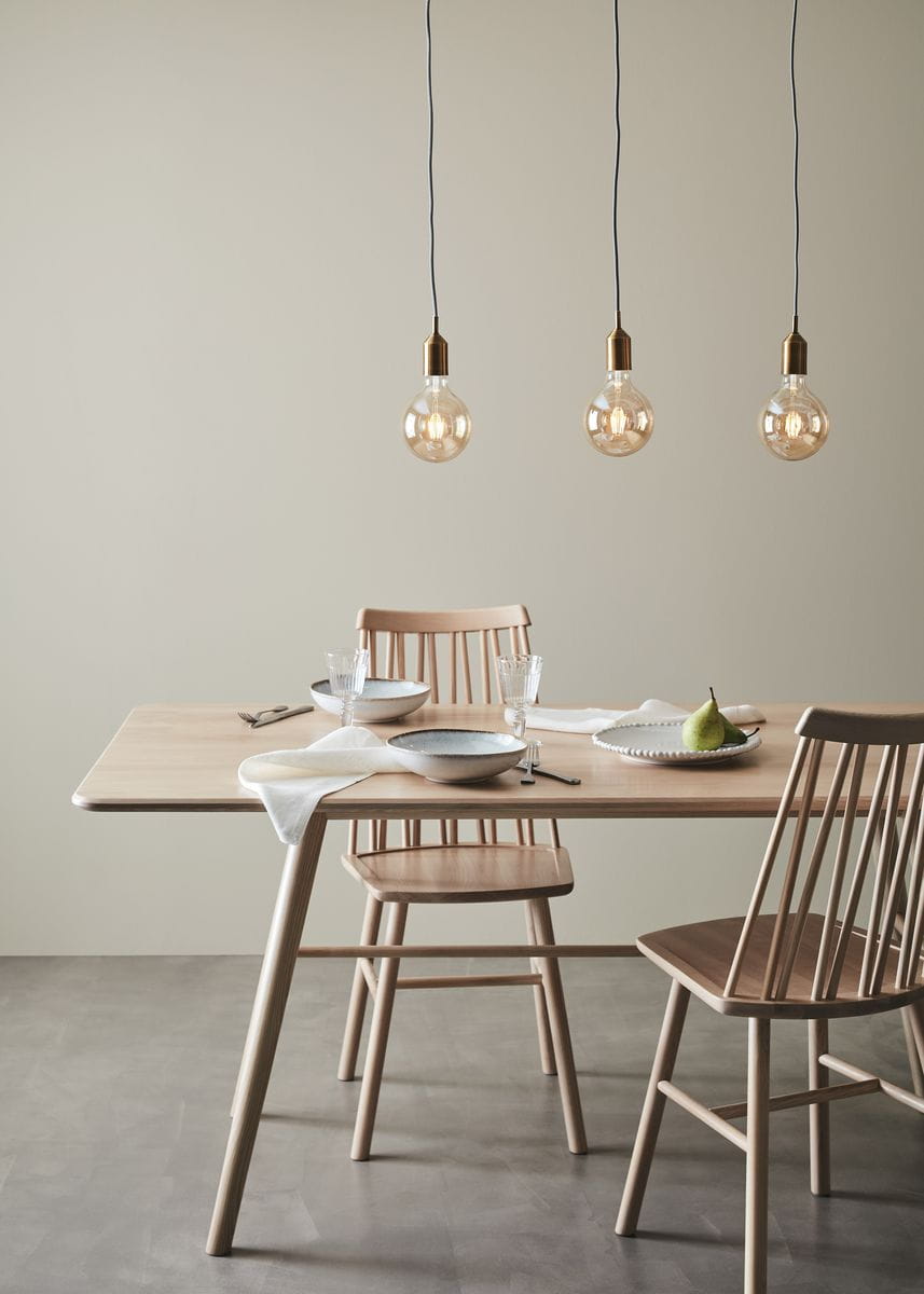 Brązowa lampa wisząca Bronx 3-punktowa z przezroczystymi kloszami, zawieszona na czarnych przewodach, umieszczona nad drewnianym stołem z ceramicznymi naczyniami i szklankami, w jasnym wnętrzu z gładką, neutralną ścianą.