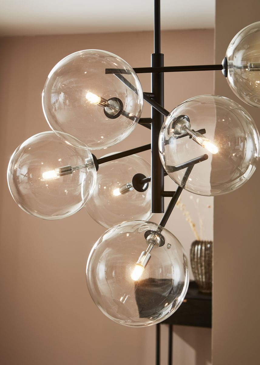 Czarna lampa wisząca Andrew z sześcioma przezroczystymi kloszami w formie kul. Klosze zawierają widoczne żarówki, umieszczone na metalowych ramionach. Produkt wisi z góry, na tle jasnej ściany, z elementami dekoracyjnymi w tle.