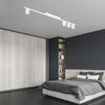 Lampa sufitowa Logan White 4-punktowa w kolorze białym, montowana na suficie w prostokątnej obudowie, z czterema okrągłymi punktami świetlnymi. Widok z dołu w nowoczesnej sypialni z szarym łóżkiem i drewnianymi akcentami na tle.