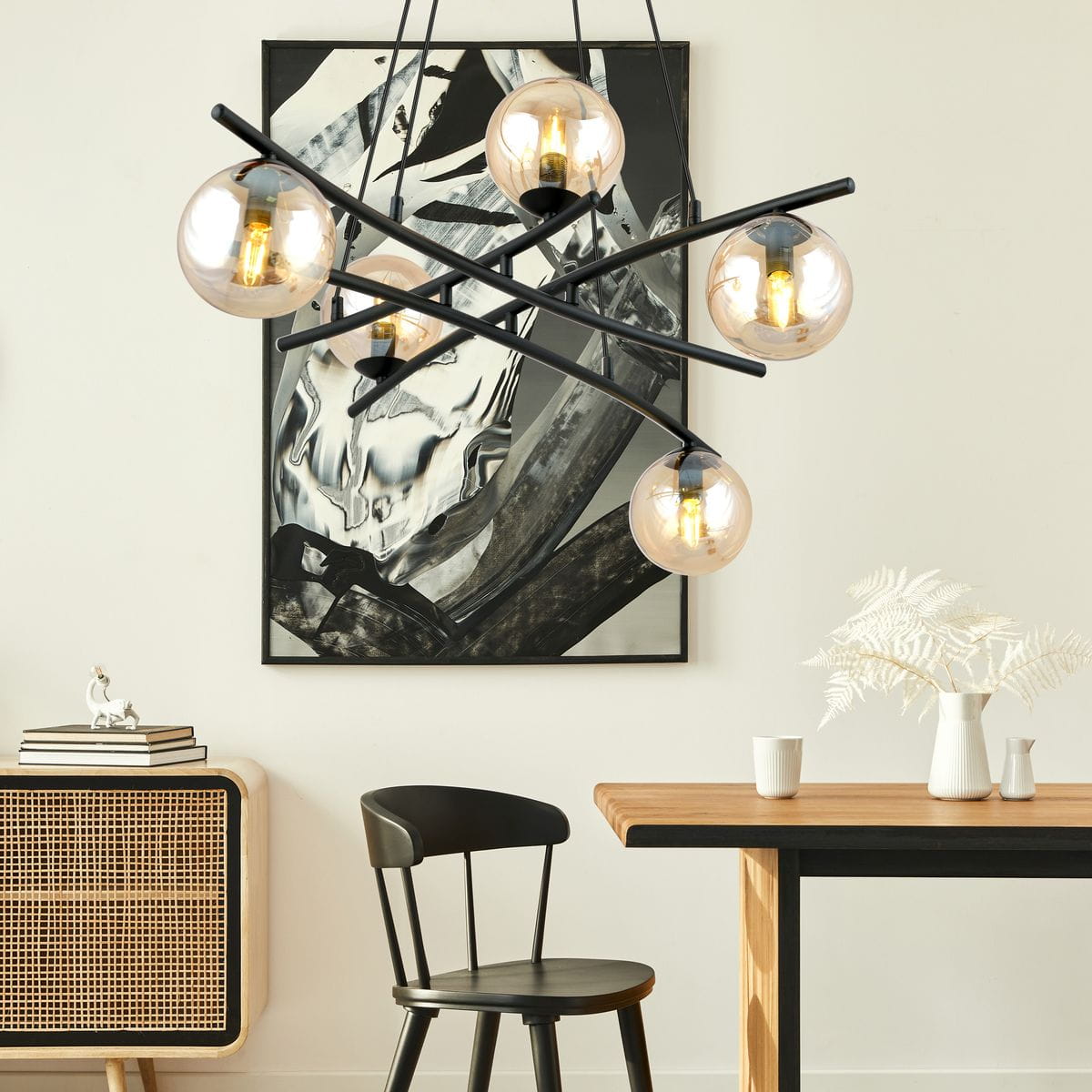 Lampa wisząca Essa 5-punktowa w kolorze czarnym z miodowymi kloszami, zawieszona w nowoczesnym wnętrzu. Klosze w kształcie kul, metalowa konstrukcja z cienkimi ramionami, umieszczona nad drewnianym stołem w towarzystwie czarnej krzesła.