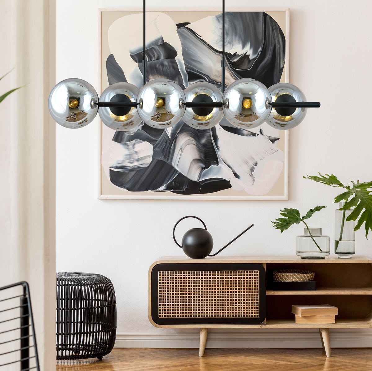 Lampa wisząca Rory 6-punktowa w kolorze czarnym i grafitowym z sześcioma metalowymi kulami w wykończeniu chromowanym, zawieszona na cienkich linkach. Produkt umieszczony w nowoczesnym wnętrzu z abstrakcyjnym obrazem w tle.