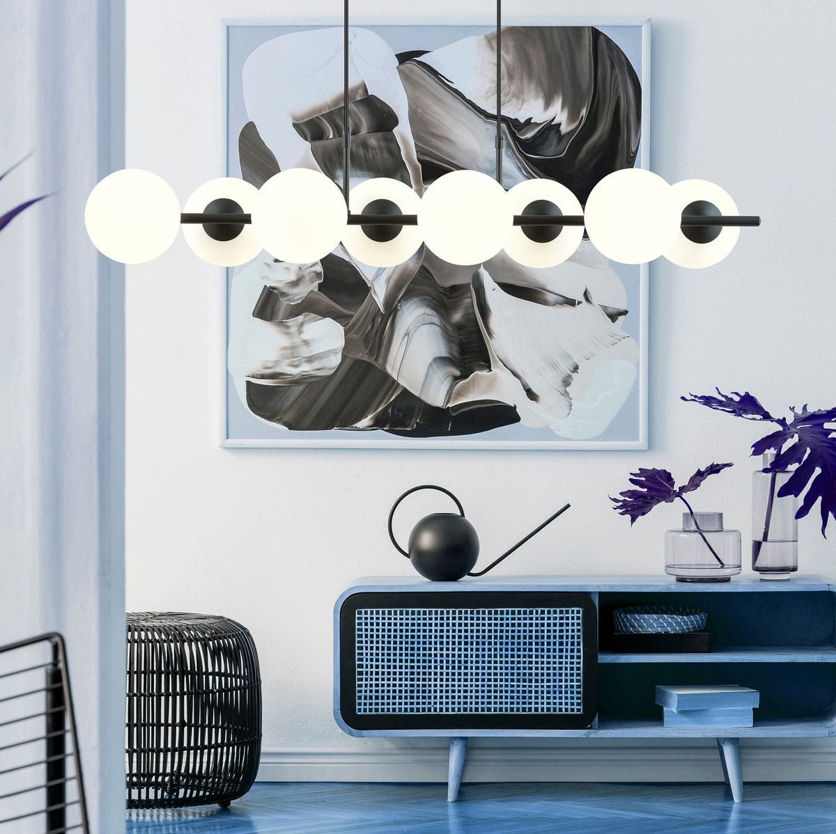 Lampa wisząca Rory 8-punktowa w kolorze czarnym z opalowymi kloszami, zawieszona poziomo nad niebieskim stolikiem. Klosze mają okrągły kształt, a całość uzupełniają nowoczesne elementy dekoracyjne w tle.