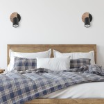 Lampa sufitowa Cover Wood (spot) 1-punktowa w kolorze czarnym, zamontowana na ścianie nad łóżkiem. Posiada okrągłą podstawę z drewna oraz cylindryczny klosz, emitujący światło. W tle widoczne poduszki i kołdra w kratę na drewnianym łóżku.