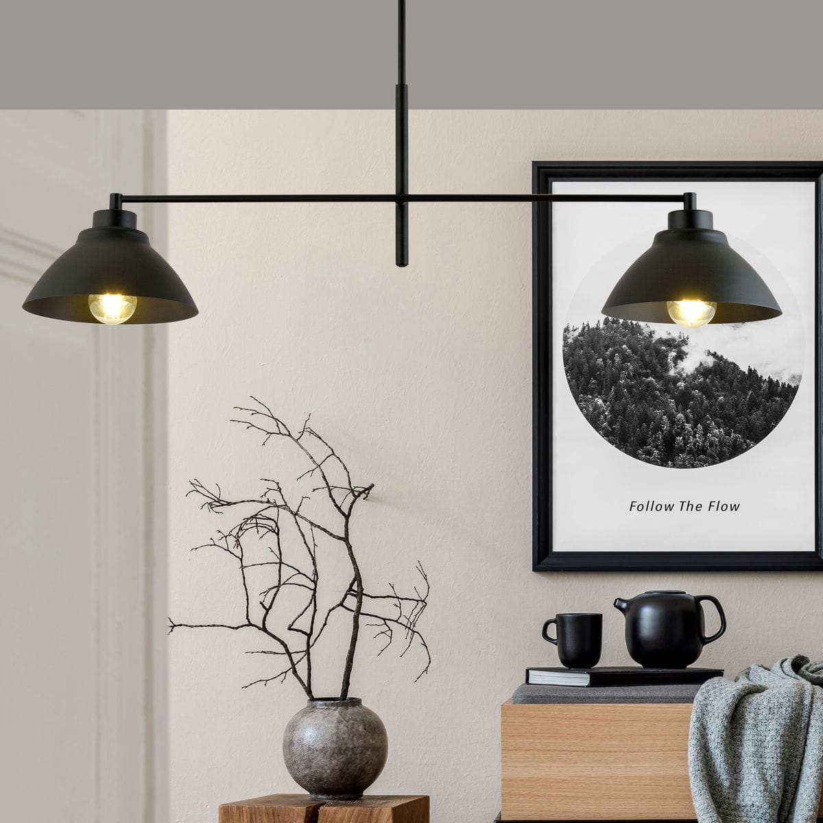Lampa wisząca 2-punktowa Maverick w kolorze czarnym, z dwoma kloszami w kształcie stożka. Ujęcie frontalne, lampa zawieszona pod sufitem, w tle dekoracyjne elementy wnętrza: obraz, wazon z gałązkami, czajnik i kubki.