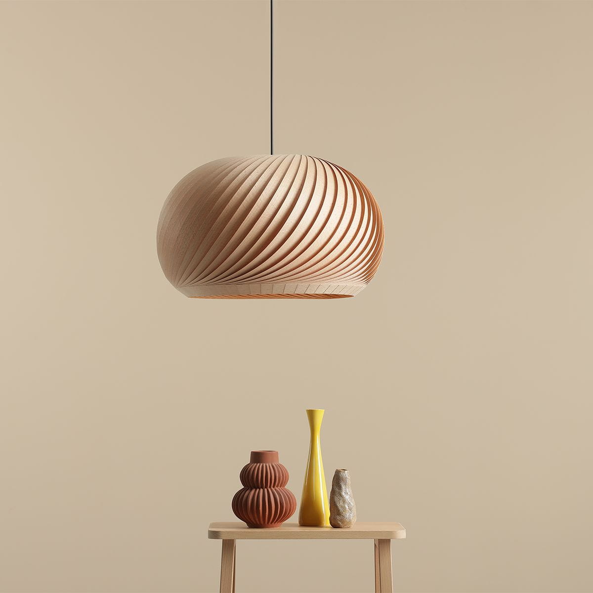 Lampa wisząca Nature Dark D45 w kształcie kulistym, wykonana z jasnego drewna, z charakterystycznym spiralnym wzorem. Zawieszona na cienkim przewodzie, w zestawieniu z dekoracyjnymi wazonami na stoliku. Tło w odcieniu beżowym.