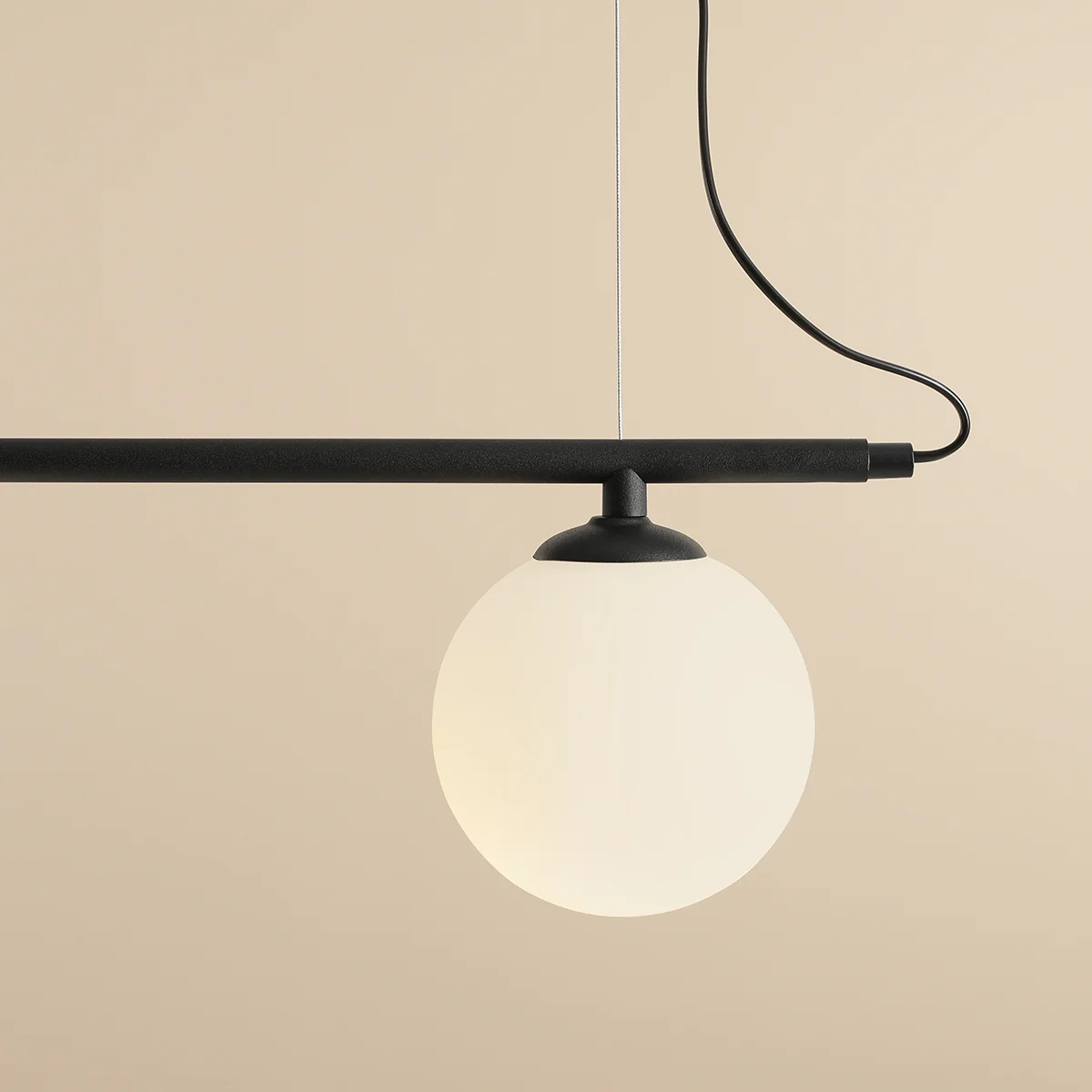 Lampa wisząca Beryl Glass 2-punktowa, czarna. Składa się z poziomego, matowego ramienia oraz okrągłej, mlecznobiałej klosza. Zawieszona na cienkim przewodzie, umieszczona na gładkim, jasnym tle. Idealna do nowoczesnych wnętrz.