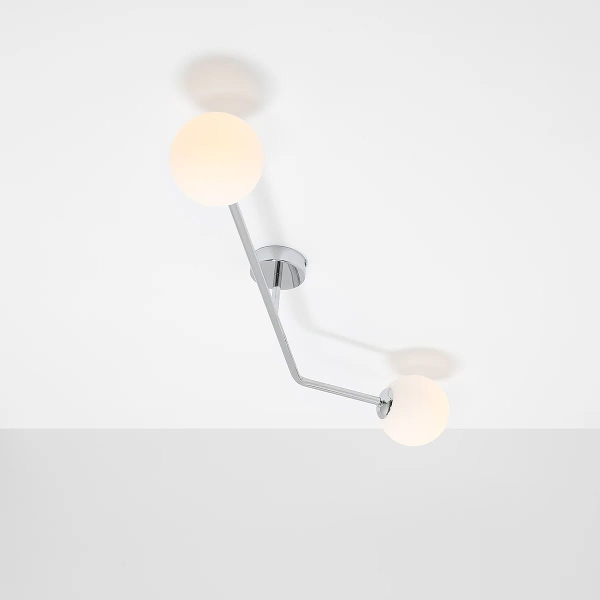 Lampa sufitowa Pure 2-punktowa w kolorze chromu. Posiada dwa okrągłe klosze z mlecznego szkła na krzyżującym się ramieniu. Montowana na suficie, z minimalistycznym designem, idealna do nowoczesnych wnętrz.