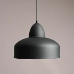 Lampa wisząca Como Black, 1-punktowa, o okrągłym kloszu w matowej czerni. Ujęcie z boku, ukazujące gładką powierzchnię i opływowy kształt. Zawieszona na cienkim przewodzie, na neutralnym tle.