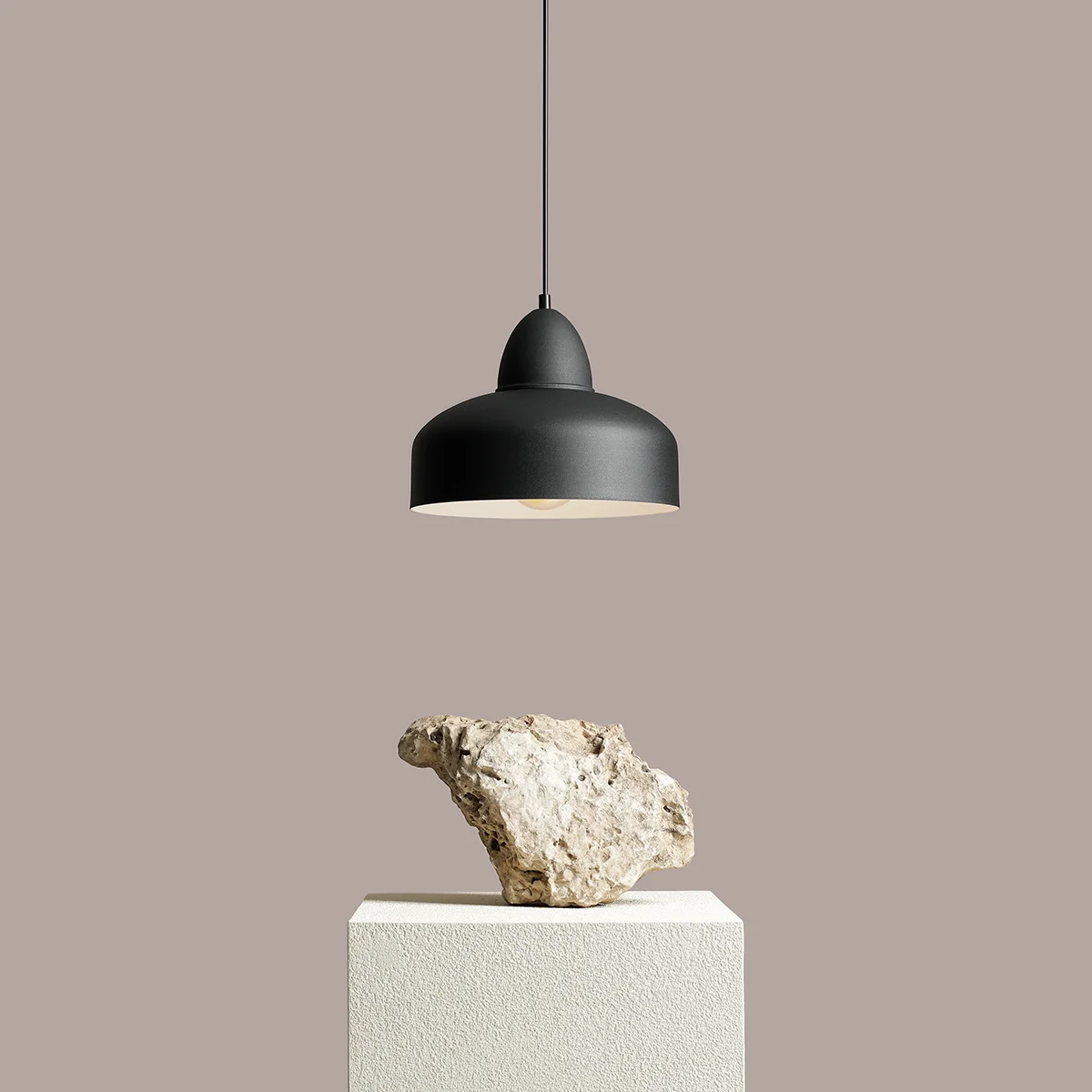 Czarna lampa wisząca Como 1-punktowa z metalowym kloszem w kształcie dzwonu. Zawieszona na cienkim kablu, z jasnym wnętrzem. Prezentowana na białym, teksturowanym postumencie, z szarym tłem. Idealna do nowoczesnych aranżacji wnętrz.