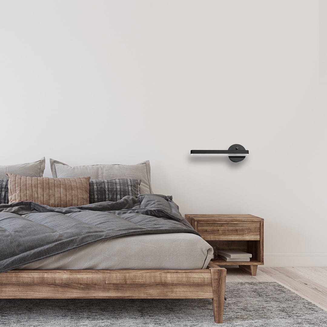 Czarny kinkiet LED Sydney 1-punktowy, lewy, o długości 30 cm i mocy 6W, zamontowany na ścianie obok łóżka w nowoczesnej sypialni, z minimalistycznym designem i okrągłą podstawą.