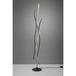 LED lampa podłogowa Blaze w kolorze mosiężnym z trzema falującymi ramionami w odcieniach czerni, bieli i złota. Stojąca na okrągłej podstawie z czarnego metalu, z kablem zasilającym na podłodze. Tło w odcieniach szarości.