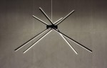Czarna lampa wisząca Spider LED z trzema punktami świetlnymi, o nowoczesnym designie. Składa się z asymetrycznych, cienkich rur LED, umieszczonych w różnych kierunkach. Montowana na suficie, idealna do nowoczesnych wnętrz. Tło w odcieniach szarości.