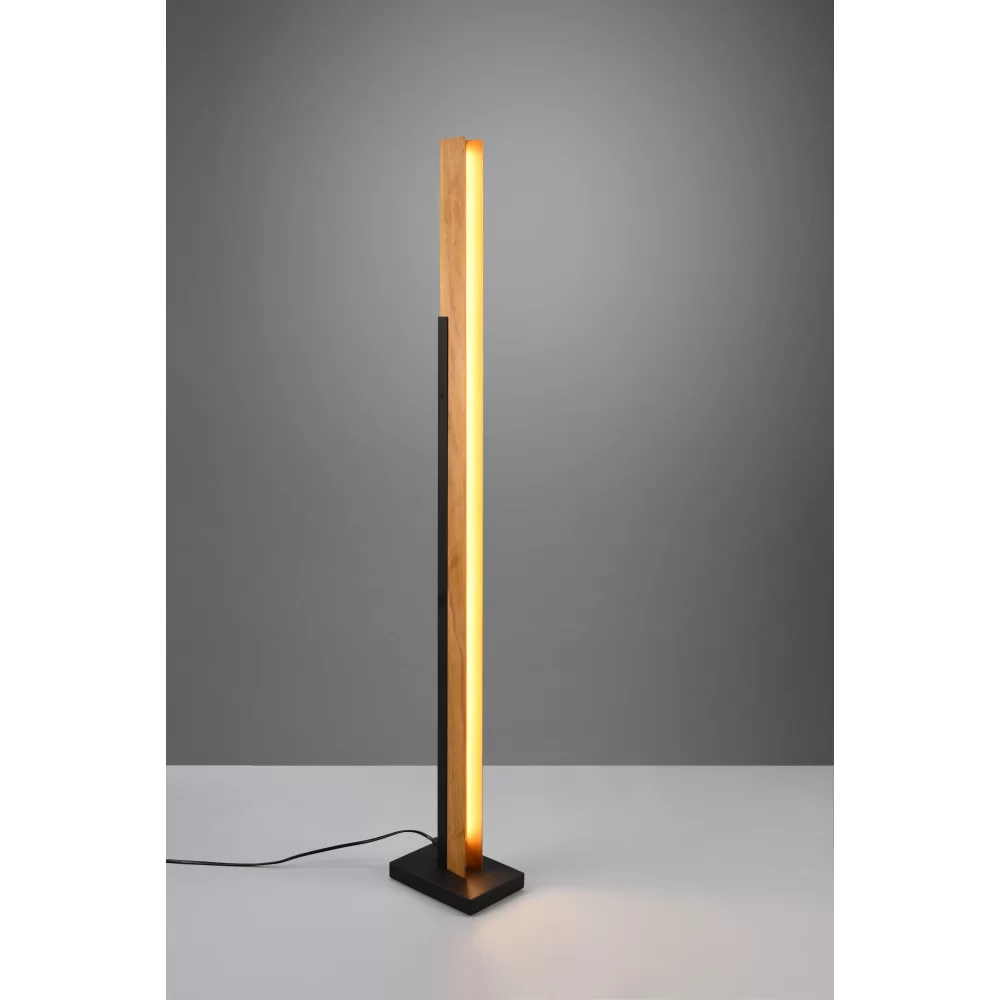 Kerala LED lampa podłogowa 1-punktowa z drewnianym słupkiem w kolorze jasnego drewna i czarną podstawą. Lampa emituje ciepłe światło, stojąca w pozycji pionowej na jednolitym tle. Kabel zasilający widoczny obok podstawy.
