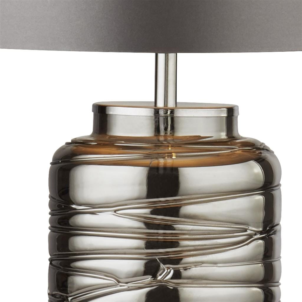 Stołowa lampa Ellie 1-punktowa z przydymionym kloszem w kolorze szarym. Baza lampy wykonana z metalicznego materiału z teksturowanym, zaokrąglonym kształtem. Lampa ma prosty, minimalistyczny design, idealna do nowoczesnych wnętrz.