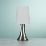 Lampa stołowa 1-punktowa w kolorze satynowego srebra z białym abażurem. Stojąca na okrągłej podstawie, o eleganckim, minimalistycznym kształcie. Ujęcie frontalne, na jednolitym tle, podkreślające nowoczesny design produktu.