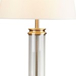 Lampa stołowa 1-punktowa w antycznym mosiądzu z kremowym abażurem. Przezroczysta, cylindryczna podstawa z metalowym detalem u góry, w zbliżeniu na detale wykończenia.