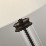 Lampa stołowa 1-punktowa w kolorze czarnym i kremowym, z przezroczystą podstawą i okrągłym, ciemnym uchwytem. Abażur z materiału w kremowym odcieniu, stojąca, w zbliżeniu na detal.