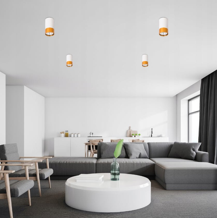 Lampa sufitowa Klemens tuba stała 1xGU10 w kolorze białym z złotym detalem, zamontowana na suficie. Widoczna w nowoczesnym wnętrzu z szarym narożnikiem i okrągłym stołem. Tło jasne, minimalistyczne, z elementami drewnianymi.