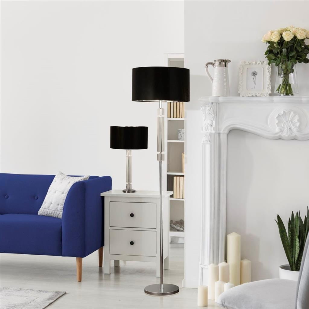 Lampa stołowa Kylie, 1-punktowa, z chromowanym stojakiem i czarnym abażurem. Ustawiona obok białej komody w jasnym wnętrzu, z niebieską sofą w tle. W pobliżu widoczne dekoracje i kwiaty.