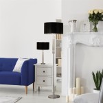 Lampa stołowa Kylie, 1-punktowa, z chromowanym stojakiem i czarnym abażurem. Ustawiona obok białej komody w jasnym wnętrzu, z niebieską sofą w tle. W pobliżu widoczne dekoracje i kwiaty.