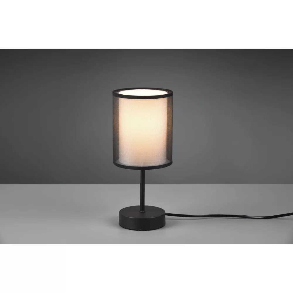 Lampa stołowa Burton, 1-punktowa, z czarnym metalowym stelażem i okrągłą podstawą. Cylindryczny klosz z białego materiału, emitujący miękkie światło. Położona na szarym tle, z widocznym kablem zasilającym.