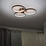 Czarna lampa sufitowa LED Groovy 3000K z trzema okrągłymi punktami świetlnymi. Widoczne dekoracyjne detale w kształcie linii oraz kryształki. Ujęcie z dołu, montowana na suficie, w tle zasłony w odcieniach szarości.
