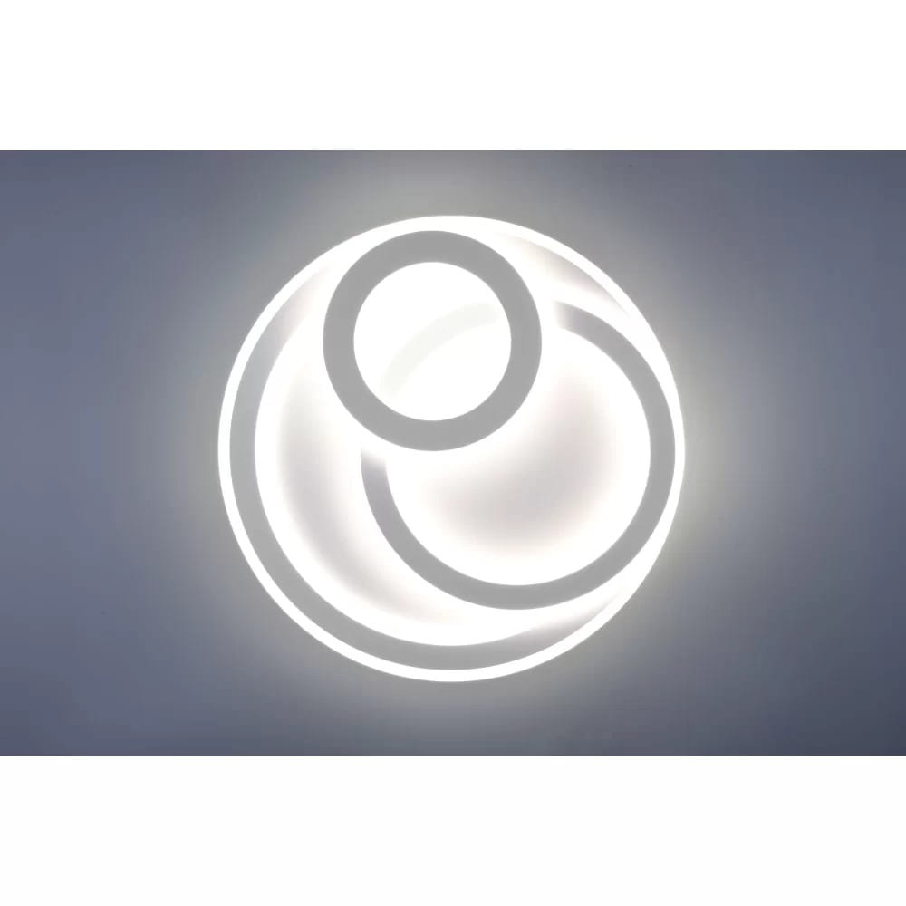 Mita LED lampa sufitowa 3-punktowa w białym kolorze, z okrągłym kształtem i dekoracyjnymi pierścieniami. Ujęcie frontalne, lampa montowana na suficie, z widocznym podświetleniem. Pilot do zdalnego sterowania w zestawie.