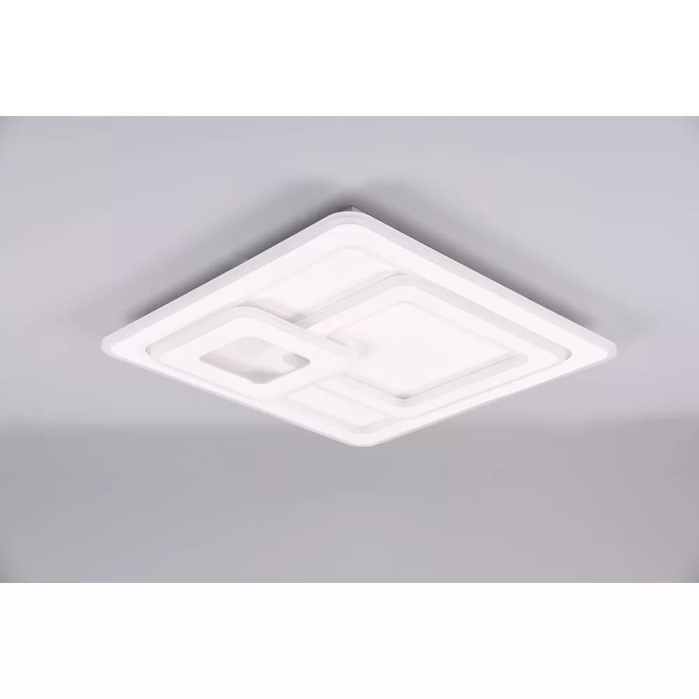Biała lampa sufitowa LED 3-punktowa z pilotem, o nowoczesnym, geometrycznym kształcie. Widok z góry, pokazujący różne poziomy i wymiary elementów. Produkt zamontowany na szarym suficie, podkreślający minimalistyczny design.