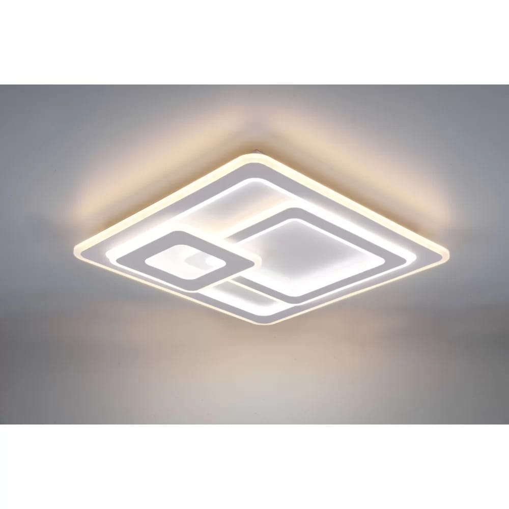 Biała lampa sufitowa LED 3-punktowa Mita z pilotem, o nowoczesnym kwadratowym kształcie, z delikatnym podświetleniem. Produkt zamontowany na suficie, z widocznymi prostokątnymi elementami. Tło jednolite, neutralne.