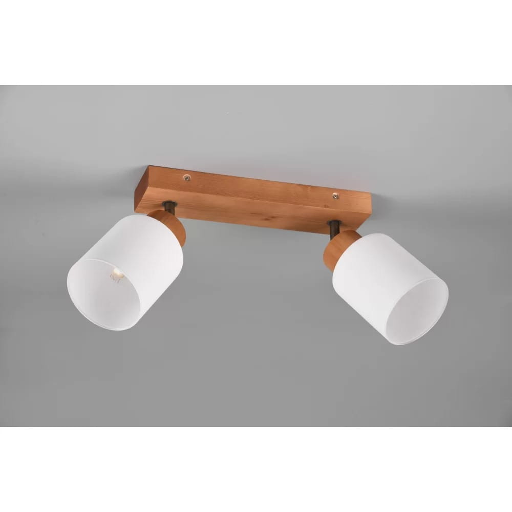 Lampa sufitowa Assam, 2-punktowa, z drewnianą podstawą w kolorze naturalnym. Posiada dwa białe klosze w kształcie cylindra, umieszczone na metalowych uchwytach. Produkt zamontowany na szarym tle.