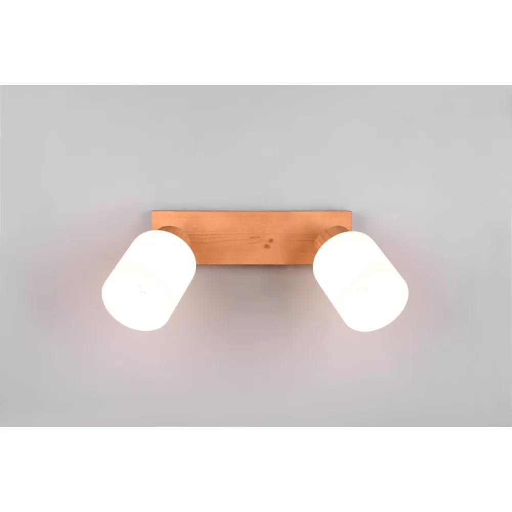 Lampa sufitowa Assam 2-punktowa z drewnianą podstawą o jasnym odcieniu, z dwoma okrągłymi kloszami w kolorze białym. Produkt zamontowany na ścianie w pozycji poziomej, oferujący nowoczesne oświetlenie. Tło w jasnym kolorze.