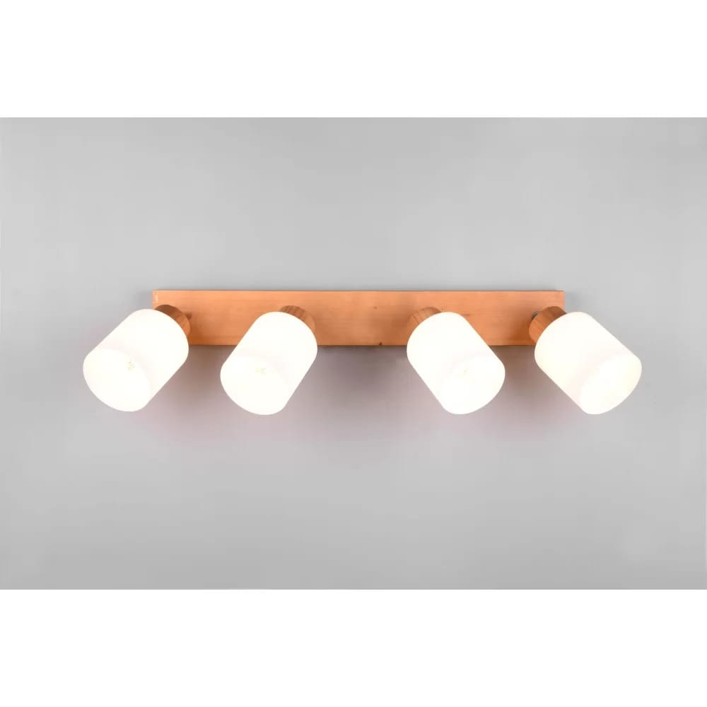 Czteropunktowa lampa sufitowa Assam z drewna, z białymi, cylindrycznymi kloszami. Ułożona poziomo, zamontowana na ścianie. Klosze skierowane w różnych kierunkach, co umożliwia regulację oświetlenia. Tło szare, minimalistyczne.
