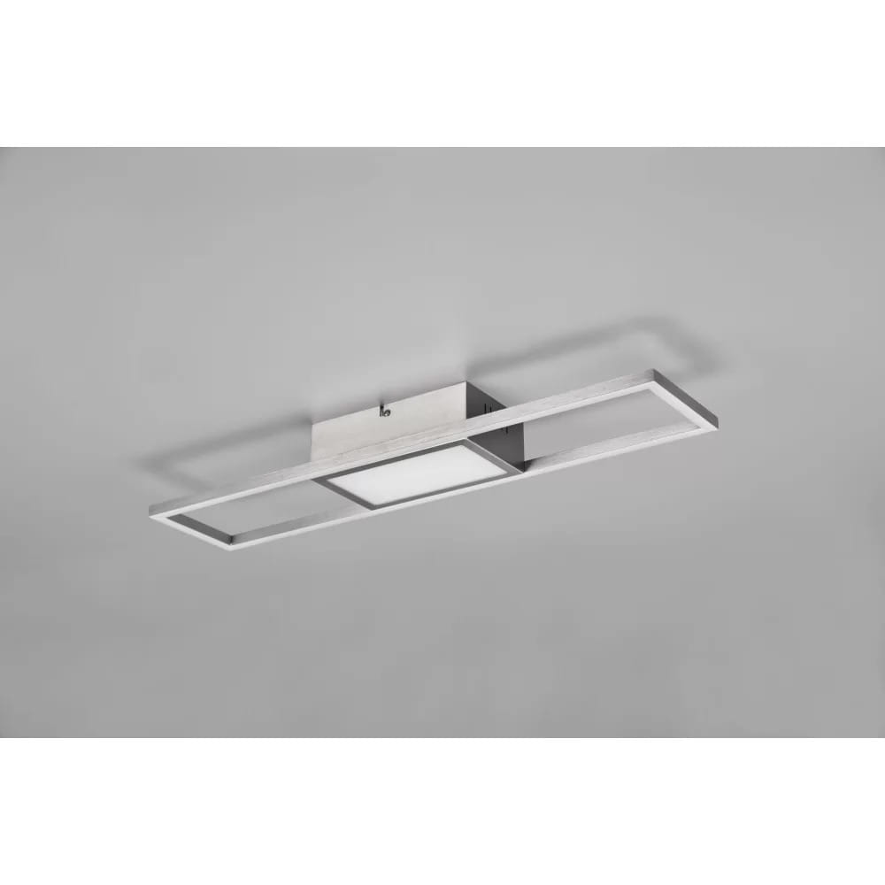 Rigido LED lampa sufitowa w kolorze niklowym, z prostokątną, matową oprawą oraz centralnym panelem świetlnym. Ujęcie z boku, zamontowana na szarym tle. Produkt z pilotem, idealny do nowoczesnych wnętrz.