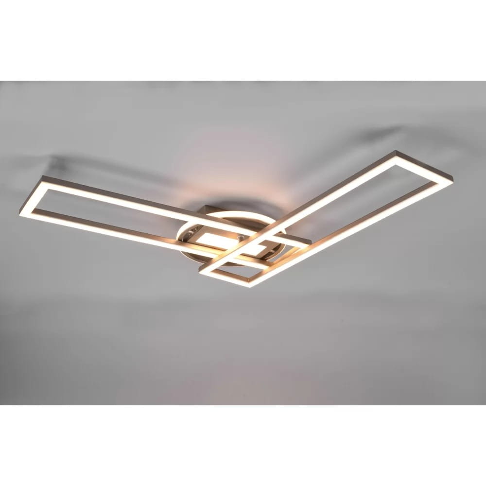 Lampa sufitowa Twister LED w kolorze niklowym z pilotem. Posiada nowoczesny design z dwiema prostokątnymi ramkami, ułożonymi w krzyż, emitującymi ciepłe światło. Zamontowana na okrągłej podstawie, z widocznymi detalami wykończenia.