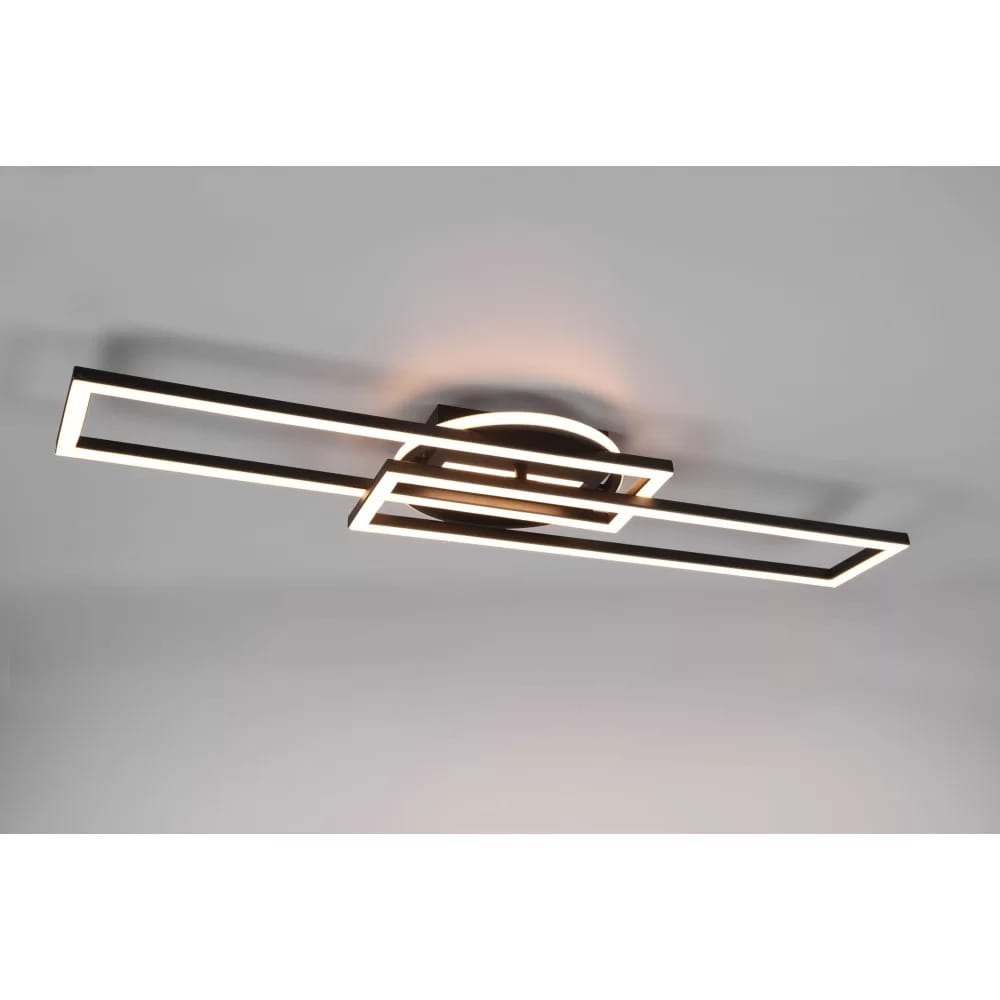 Czarna lampa sufitowa Twister LED z pilotem, o nowoczesnym designie, składająca się z prostokątnych ram w kształcie litery L. Zamontowana na okrągłej podstawie, emitująca ciepłe światło, idealna do nowoczesnych wnętrz.