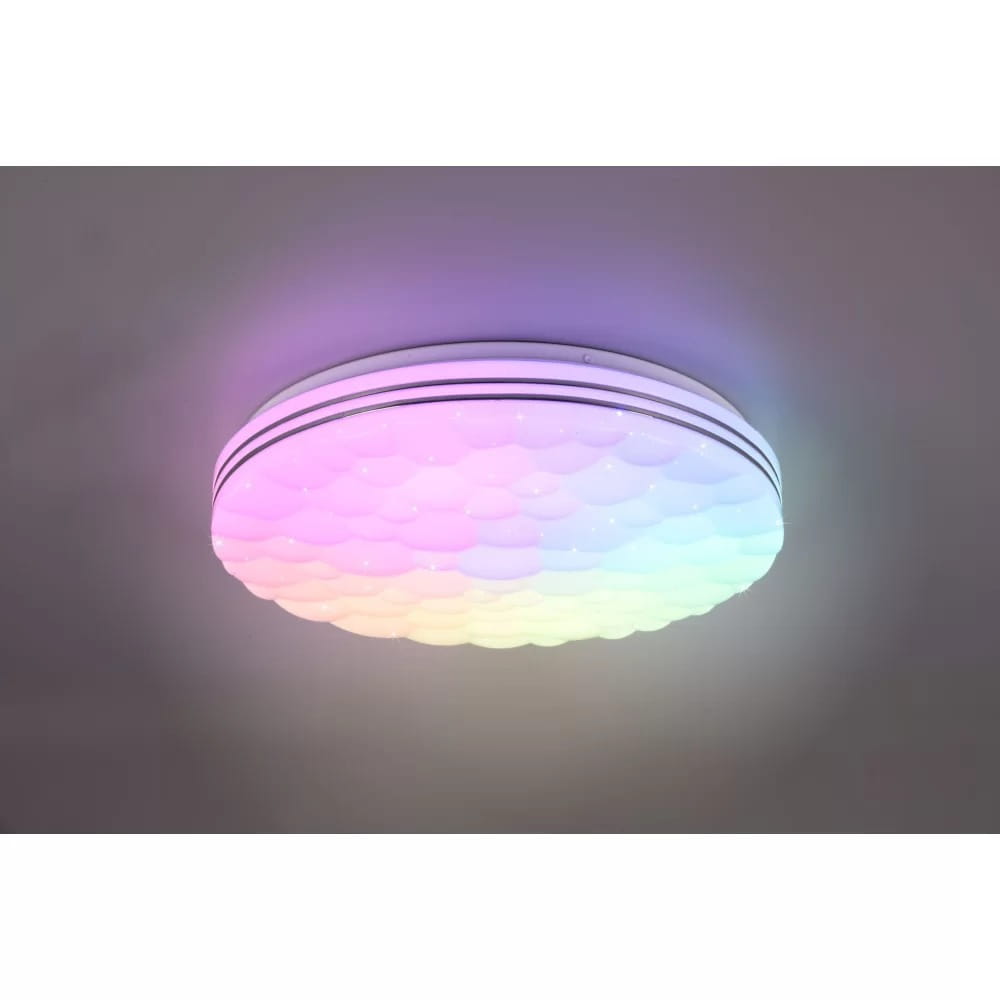 Plafon LED Tiger w kolorze białym z pilotem, o okrągłym kształcie, z dekoracyjną, teksturowaną powierzchnią. Emituje wielokolorowe światło RGB w odcieniach różu, niebieskiego i zielonego. Zamontowany na suficie, widoczny z góry.