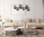 Lampa wisząca Canello w kolorze czarnego chromu z dymionymi kulami, zawieszona nad sofą w jasnym wnętrzu. Osiem kul w różnych rozmiarach na prostym stelażu, tworzy nowoczesny akcent w aranżacji. Tło w odcieniach beżu i bieli.