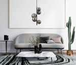Lampa wisząca Canello, 5-punktowa, w kolorze czarnego chromu z dymionymi kloszami, zawieszona nad stolikiem kawowym. W tle szara sofa, roślina i minimalistyczna dekoracja na ścianie.