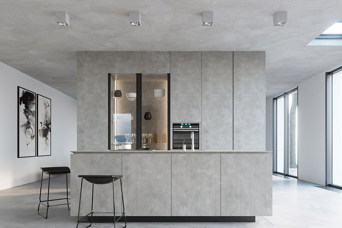 Lampa sufitowa Valde 1-punktowa w betonowej obudowie, zamontowana na suficie w nowoczesnej kuchni. Kąt ujęcia frontalny, z widokiem na minimalistyczne wnętrze z szarymi ścianami i dużymi oknami. W tle widać także czarne stołki i szafki.