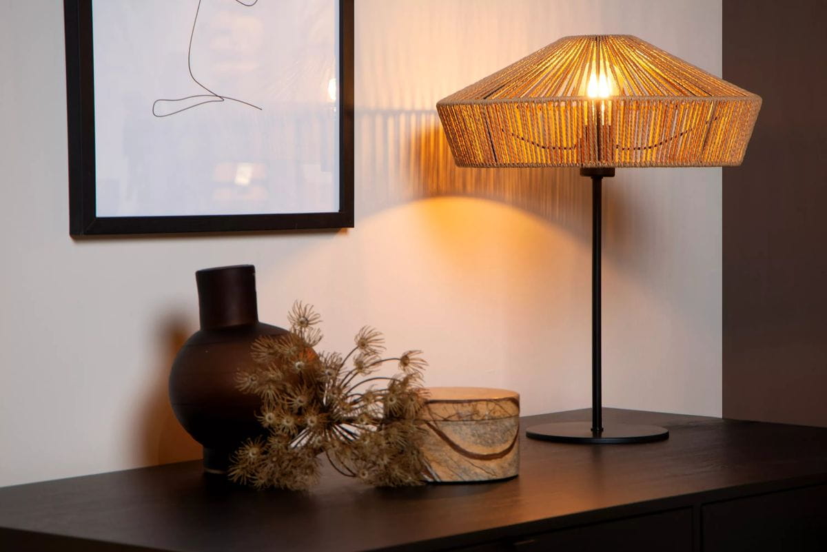 Lampa stołowa Yunkai 1-punktowa w kolorze czarnym z jasnym drewnem, z kloszem z cienkich pasków, stojąca na czarnej podstawie. Obok widoczne ciemna waza i dekoracyjna drewniana skrzynka. Tło w jasnych odcieniach.
