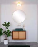 Lampa sufitowa Trudy 3-punktowa w kolorze złotym z trzema okrągłymi kloszami w białym kolorze. Miejsce montażu na gładkiej, jasnej ścianie, otoczenie z lustrem w złotej ramie i minimalistycznym umeblowaniem w łazience.