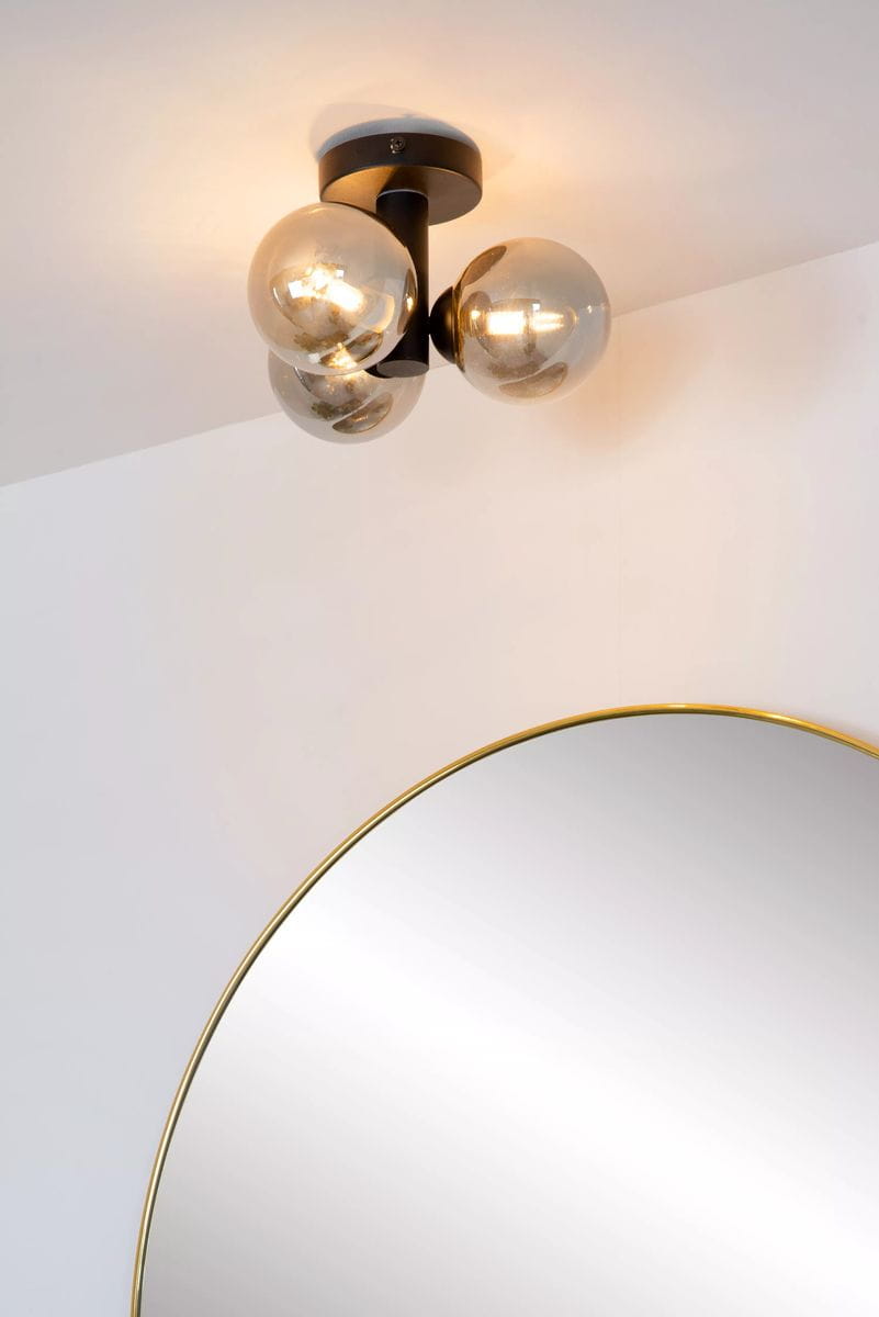Czarna lampa sufitowa Trudy 3-punktowa, z trzema okrągłymi kloszami w kolorze złotym, zamontowana na suficie. Widok z dołu, lampa o nowoczesnym designie, w tle okrągłe lustro z złotą ramą.