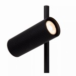 Czarna lampa stołowa 1-punktowa Clubs z cylindrycznym kloszem o żłobionej fakturze, zamontowana na prostej, smukłej nodze. Klosz skierowany w dół, emitujący ciepłe światło. Produkt w minimalistycznym stylu, na białym tle.