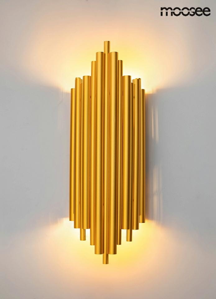 Kinkiet Harmonic 2-punktowy w złotym kolorze, wykonany z metalowych rur o teksturowanej powierzchni, montowany na ścianie. Emituje światło w górę i w dół, tworząc efektowne oświetlenie. Prosty, nowoczesny design, umieszczony na jasnym tle.